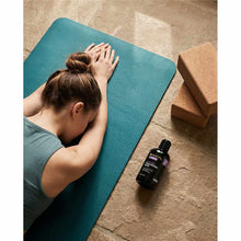 Black bottle of Baxyl Healthy Joints supplement on concrete floor next to blue yoga mat with person.