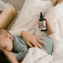 Person holding Lactivist dropper bottle with nursing brush nearby on white bedding.