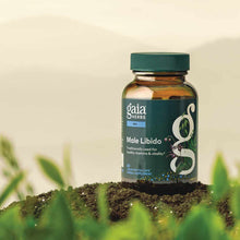 Gaia Herbs Male Libido supplement bottle with green cap and dark label, sitting on soil with green plants in background.