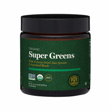 Dark glass jar with black lid containing green-labeled Organic Super Greens powder with certification logos.