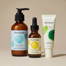 Three Mad Hippie skincare products: amber pump bottle of Cream Cleanser, brown dropper bottle of Vitamin C Serum, and white t