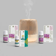 Wooden ribbed diffuser with mist output surrounded by four boxed essential oil bottles labeled Mental Clarity, Peace, and Dow