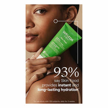Person holding green Weleda Skin Food tube near their face, displaying product and hydration claim text.
