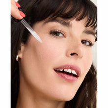 Person applying clear facial serum with a dropper near the eye area.