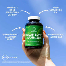 Hand holding dark glass bottle of MRM Vegan Bone Maximizer capsules with white cap against blue background.