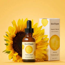 Mad Hippie Vitamin C Serum in amber glass bottle with dropper, displayed with product box and sunflower on yellow background.