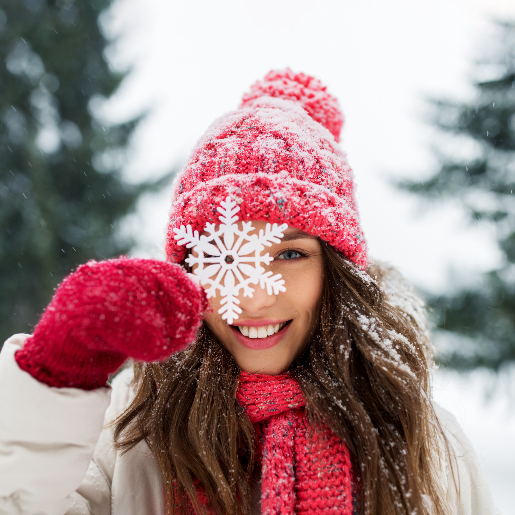 A women outdoors bundled up in snowy weather putting a large snowflake in front of her face