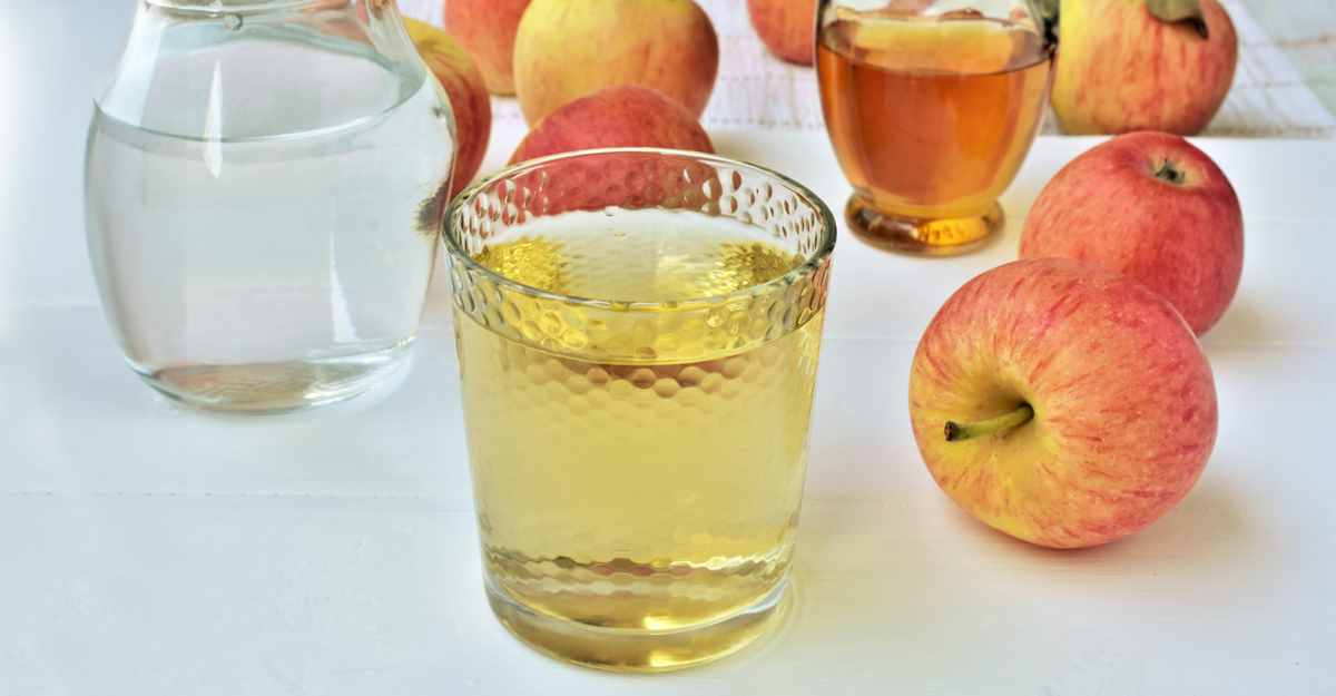 A glass of apple juice with apples around it