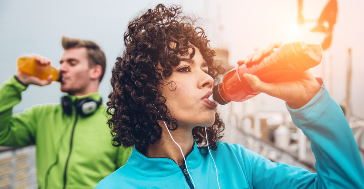 A young man and women drinking water while on a run outside
