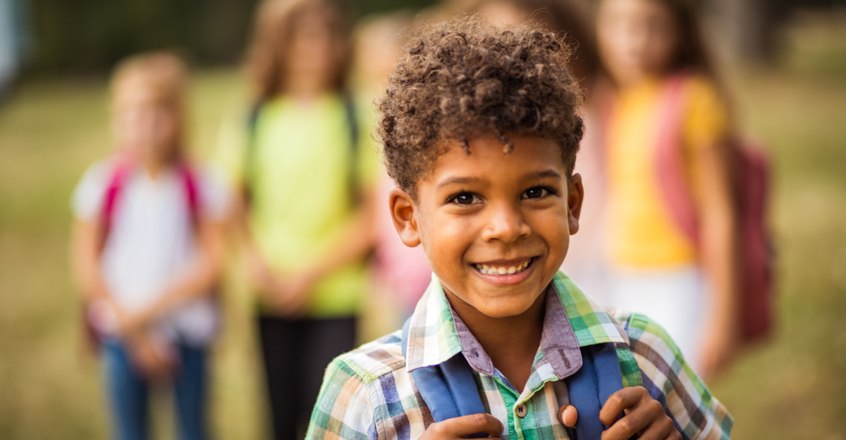 A little kid smiling with a backpack on