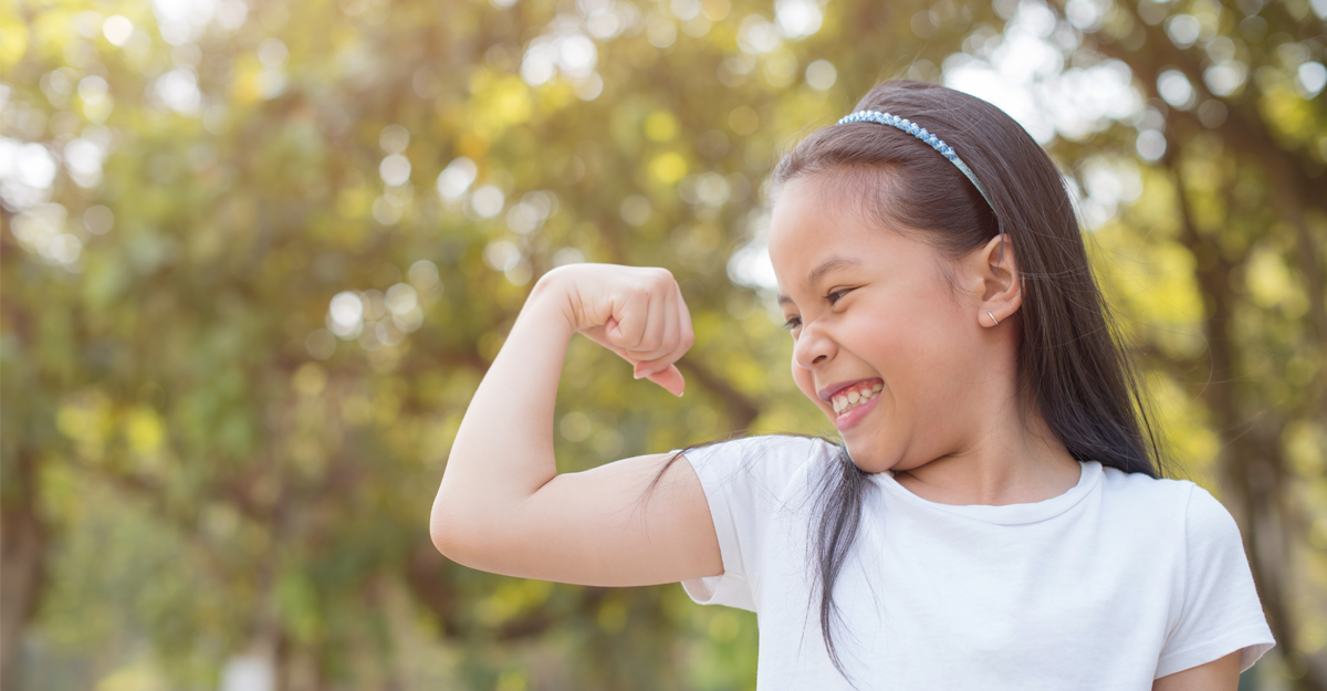 A young girl smiling making a muscle with her arm outdoors