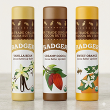 Three Badger cocoa butter lip balm tubes in vanilla bean, creamy cocoa, and sweet orange flavors with illustrated botanical l