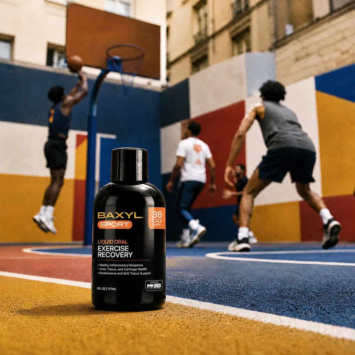 Black bottle of Baxyl Sport liquid oral exercise recovery supplement on outdoor basketball court with players in background.