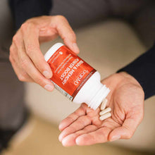 White capsules dispensing from red and white BrainMD supplement bottle held in hand.