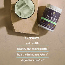 Ancient Nutrition Colostrum powder in Coconut Lime flavor with scoop and prepared drink on stone surface.