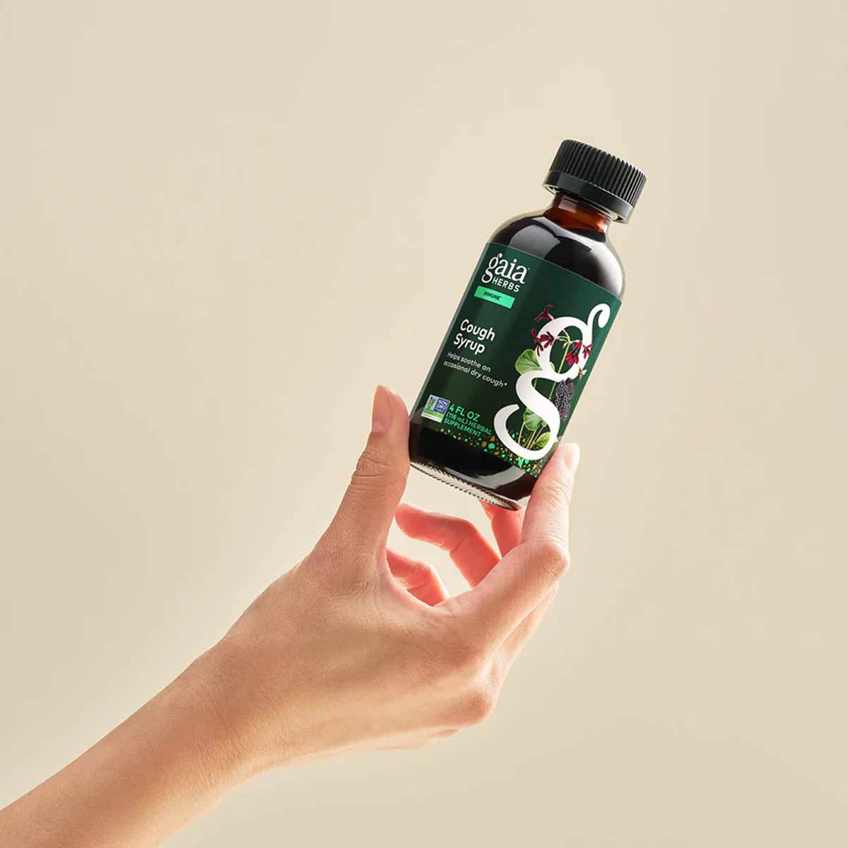 Gaia Herbs Cough Syrup dark glass bottle with black cap held in hand against beige background.