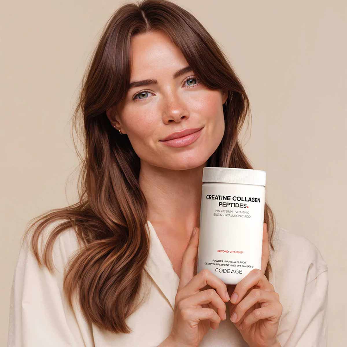 Woman holding white Codeage Creatine Collagen Peptides container with ingredient list visible on label.