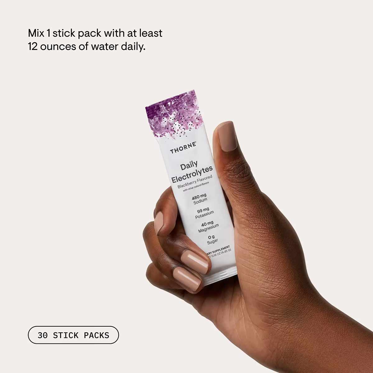 Hand holding white Thorne Daily Electrolytes stick pack with purple sparkling top and blackberry flavor label.
