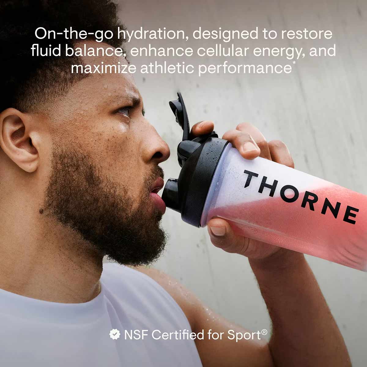 Man drinking from pink Thorne electrolyte bottle with black cap during exercise.