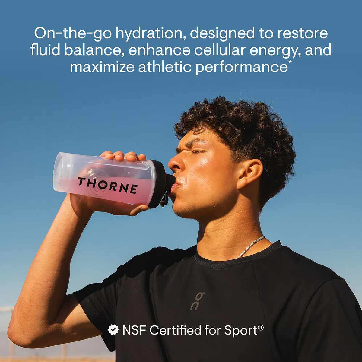 Man drinking from pink Thorne electrolyte bottle against blue sky.
