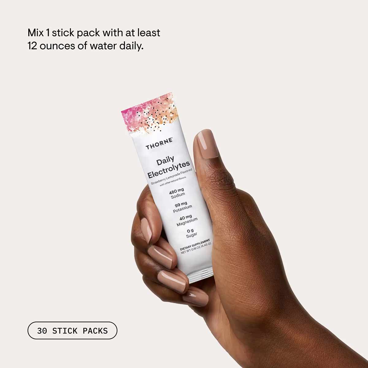 White stick pack of Thorne Daily Electrolytes with pink watercolor top design, held in hand.