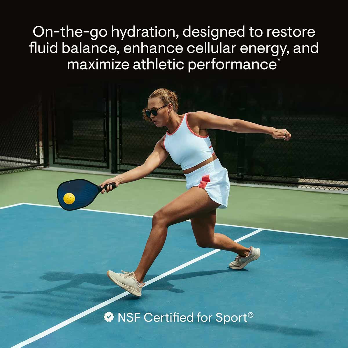 Athlete playing pickleball on court wearing light blue sports top and skirt with white sneakers.