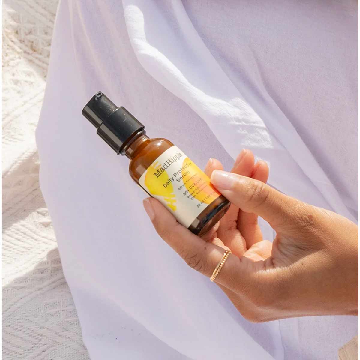 Amber glass bottle with black pump top held in hand against lavender fabric background.