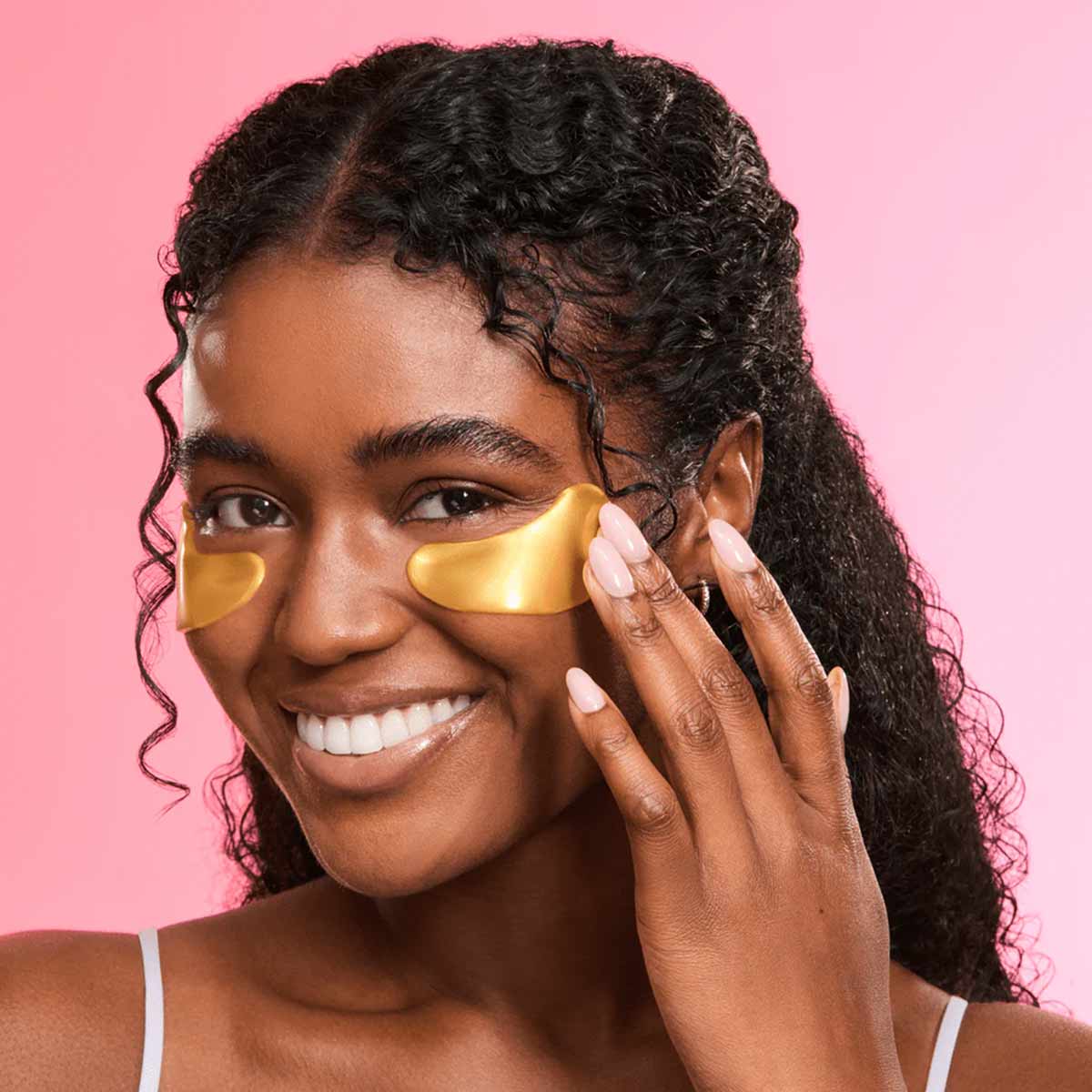 Person wearing gold under-eye masks on pink background.