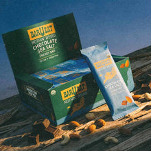 Green BAR U EAT display box and individual chocolate sea salt energy bar packet on driftwood at beach.
