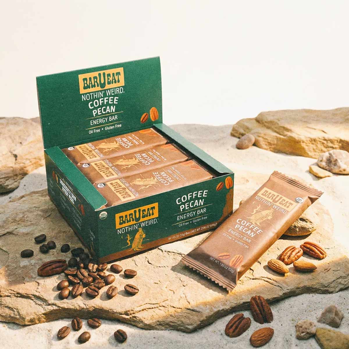 Green BAR U EAT display box with Coffee Pecan energy bars, individual wrapper, coffee beans, and pecans on sandy surface.