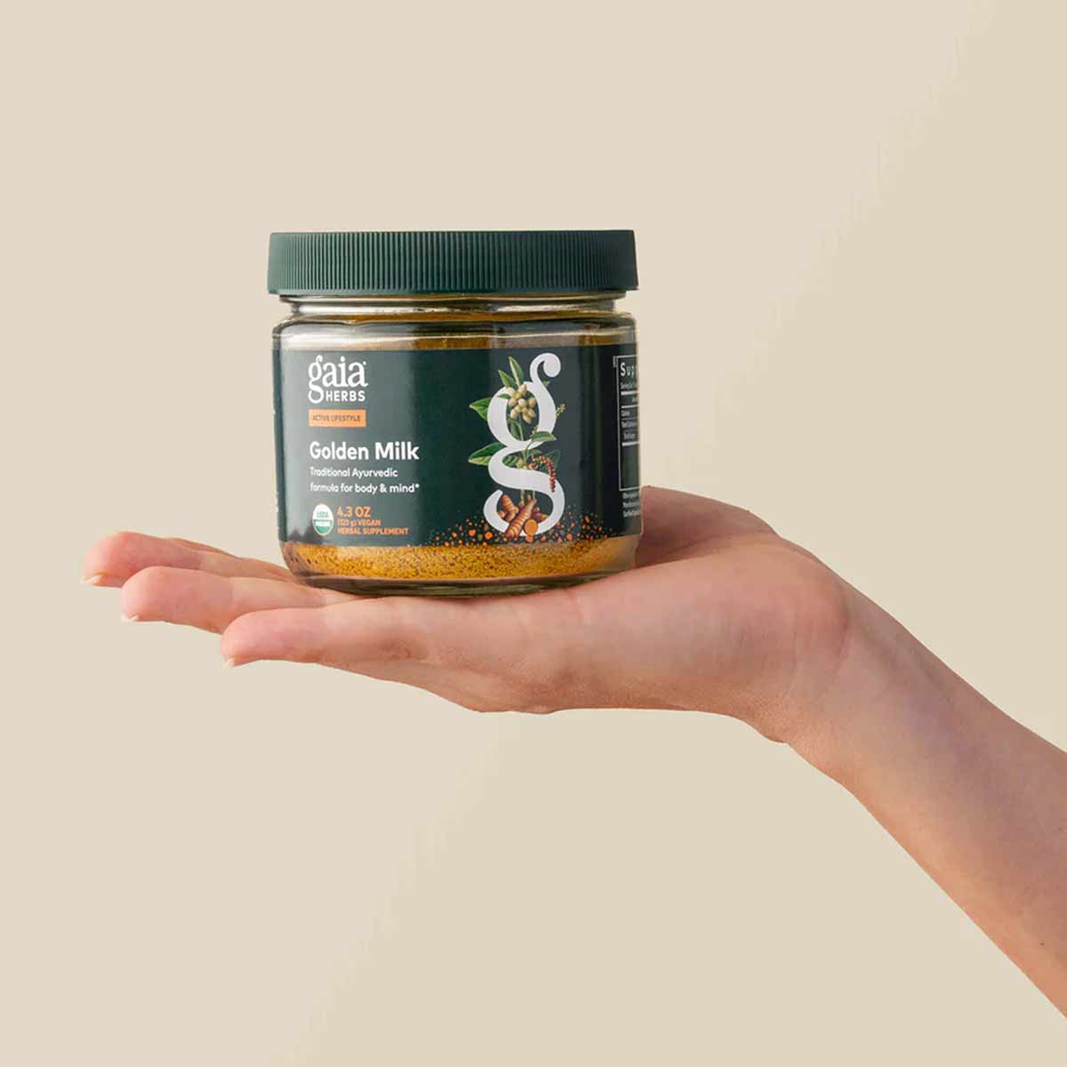 Gaia Herbs Golden Milk powder in 4.3 oz glass jar with green lid, held in an open palm.