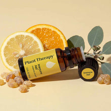 An amber bottle with a yellow Plant Therapy Immune Aid label lies beside lemon and orange slices, resin pieces, and eucalyptus leaves.