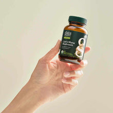 Hand holding amber glass bottle of Gaia Herbs Lion's Mane Mushroom supplement with dark green cap and black label.