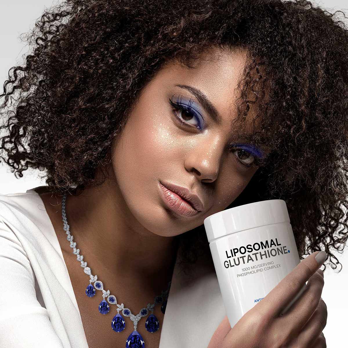 White container labeled "Liposomal Glutathione" held by a person wearing a white top and blue gemstone necklace.