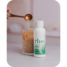 Rho Nutrition liposomal glutathione supplement bottle next to a glass of liquid with a bronze spoon drizzling product.