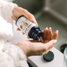 Hand holding dark blue glass bottle with white label and capsules spilling into palm.