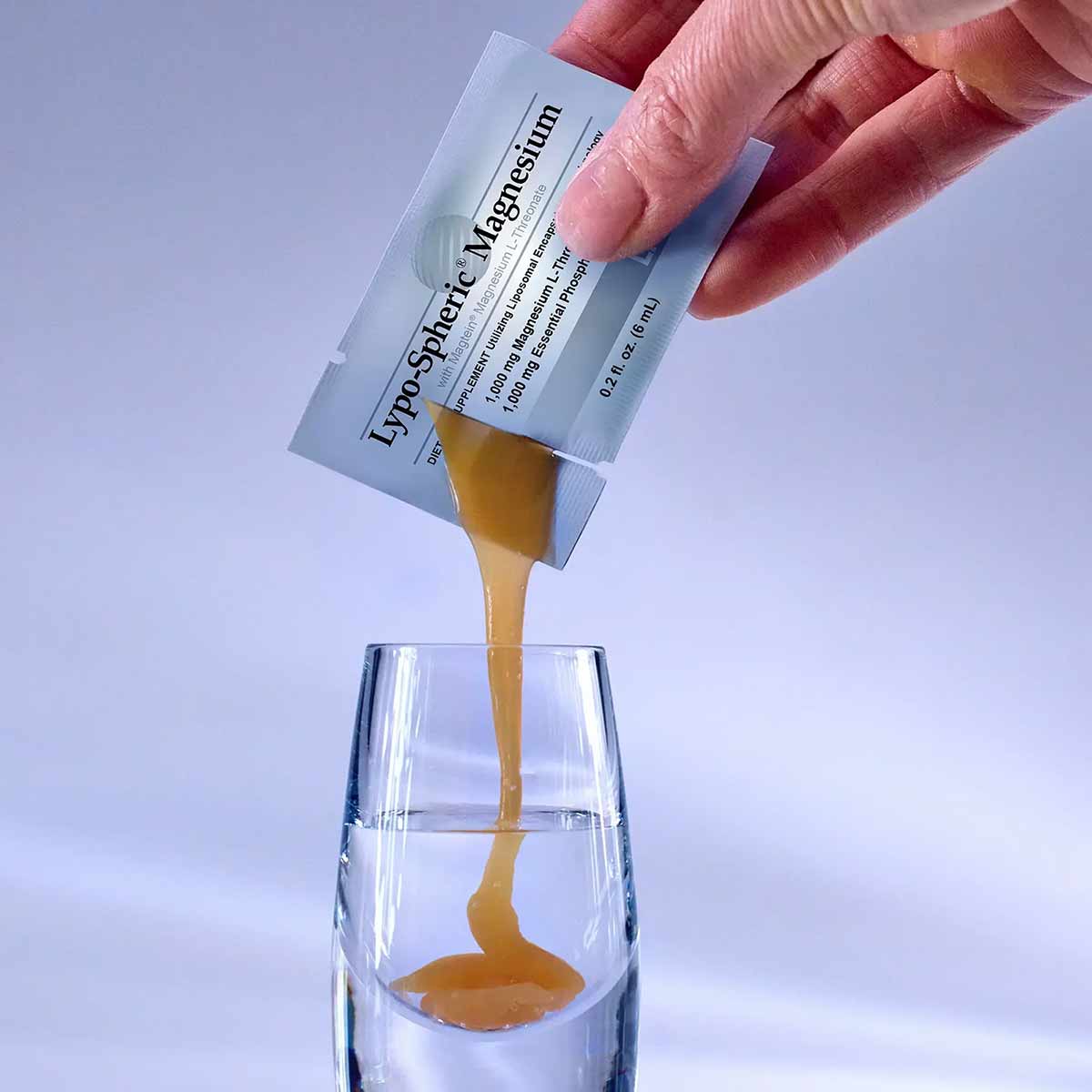 Hand pouring golden liquid from Lypo-Spheric Magnesium packet into a glass of water.