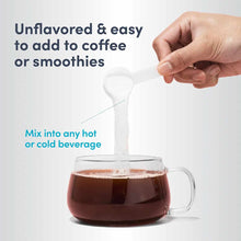 Hand holding white scoop pouring powder into glass mug of dark beverage.