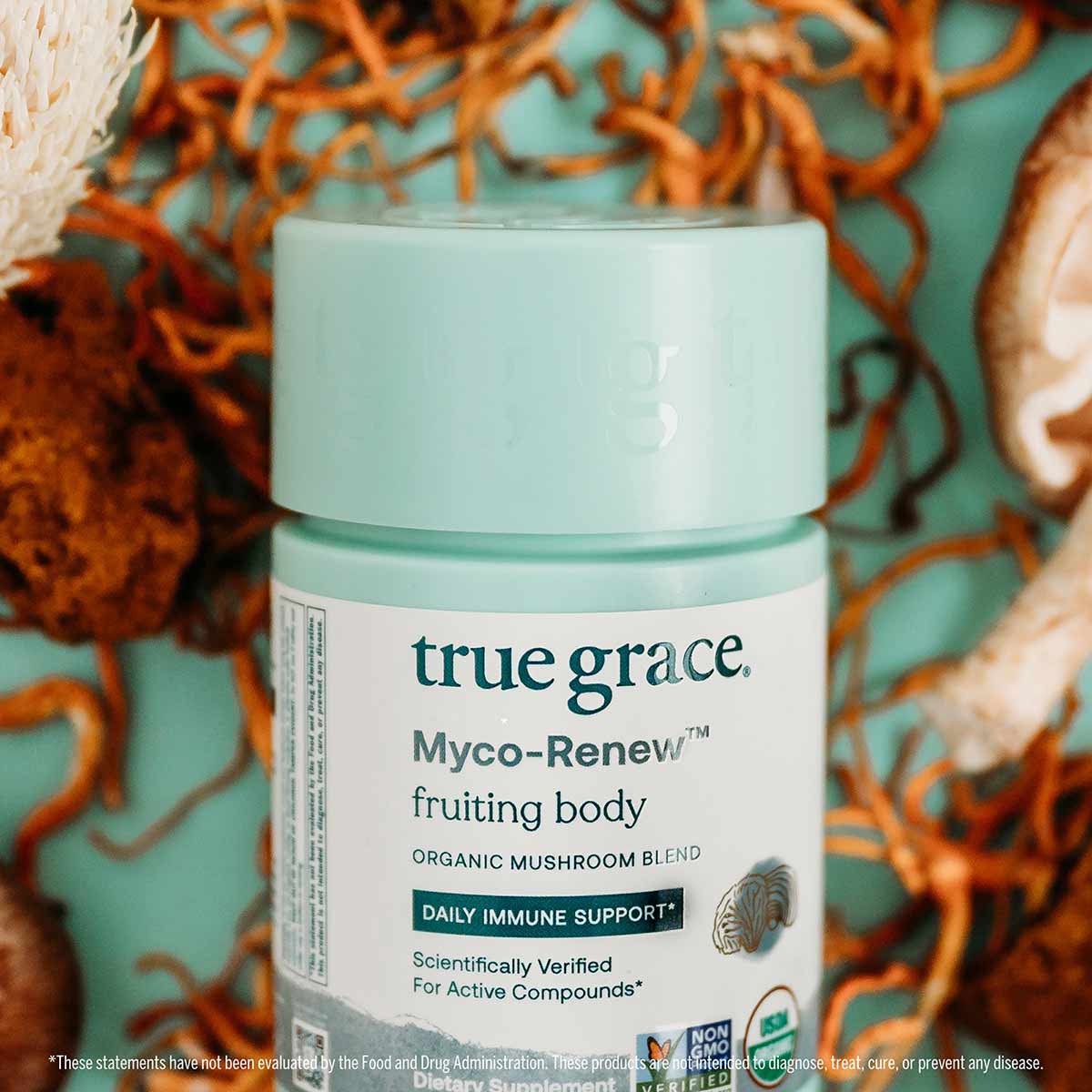 Light blue jar of True Grace Myco-Renew fruiting body organic mushroom blend supplement with label visible, surrounded by dri