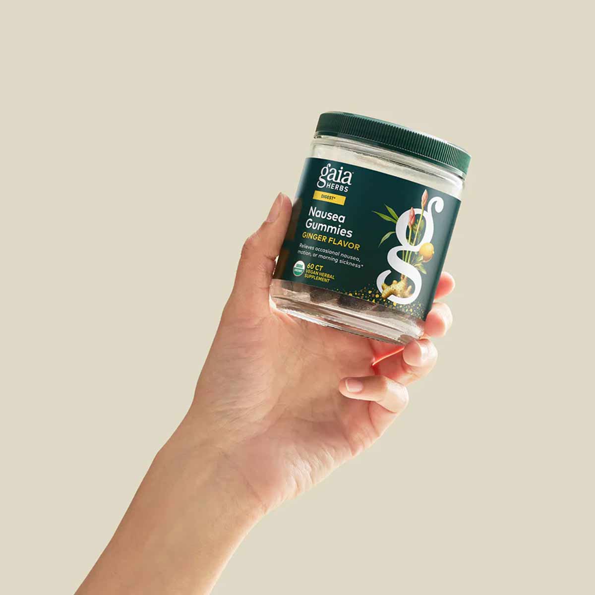 Hand holding clear glass jar of Gaia Herbs Nausea Gummies with ginger flavor label and green cap.