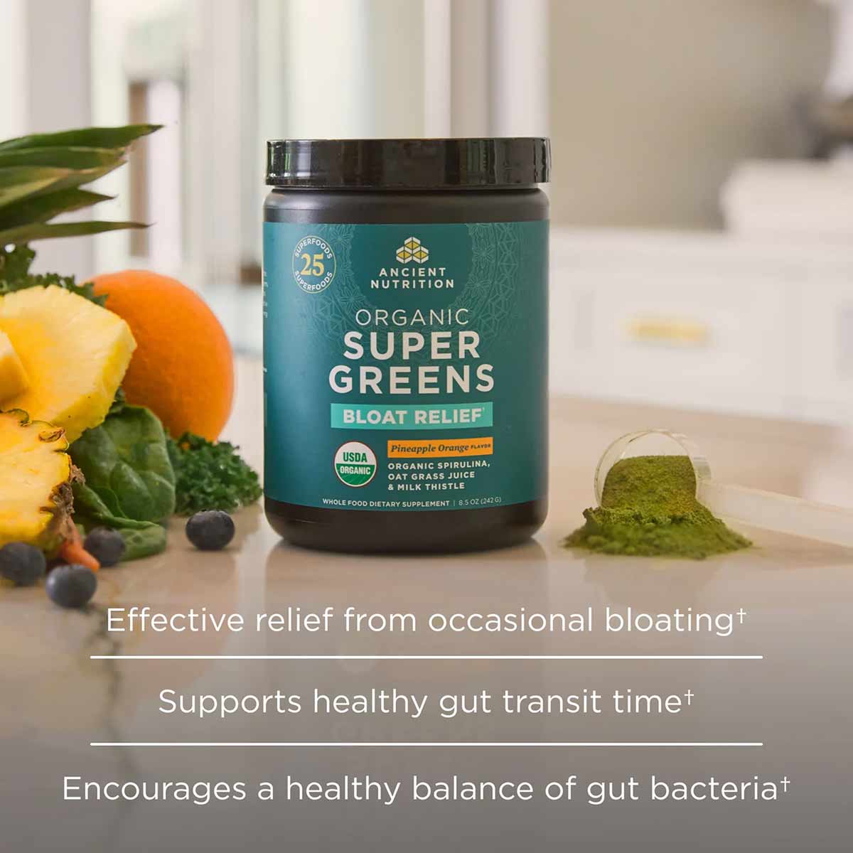 Dark glass jar of Organic SuperGreens + Bloat Relief powder with teal label, surrounded by pineapple, blueberries, and green 