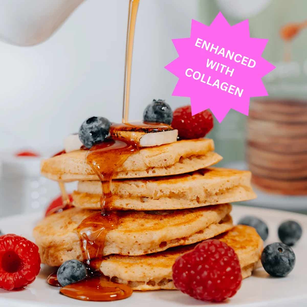 A stack of golden pancakes topped with banana slices, blueberries and raspberries has syrup pouring over it, beside a pink "Enhanced with Collagen" badge.