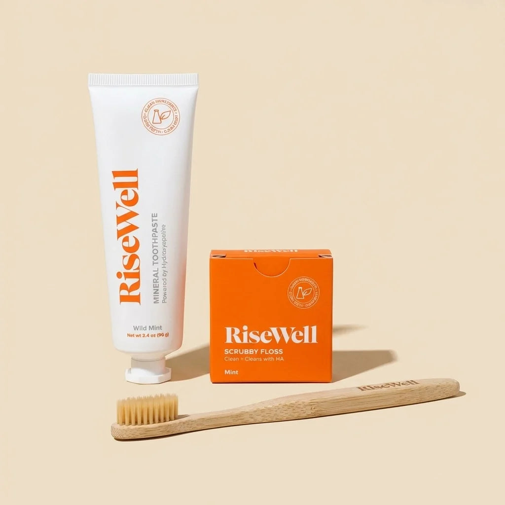 RiseWell toothcare bundle containing white tube of Wild Mint toothpaste, orange box of Scrubby Floss, and wooden toothbrush w