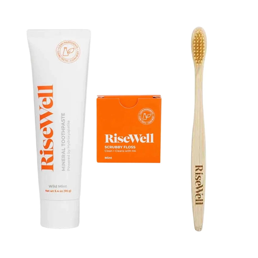 RiseWell toothcare bundle containing white mineral toothpaste tube, orange scrubby floss box, and wooden toothbrush with yell