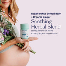 Woman holding True Grace Prenatal Multivitamin bottle with fresh flowers against pink background.