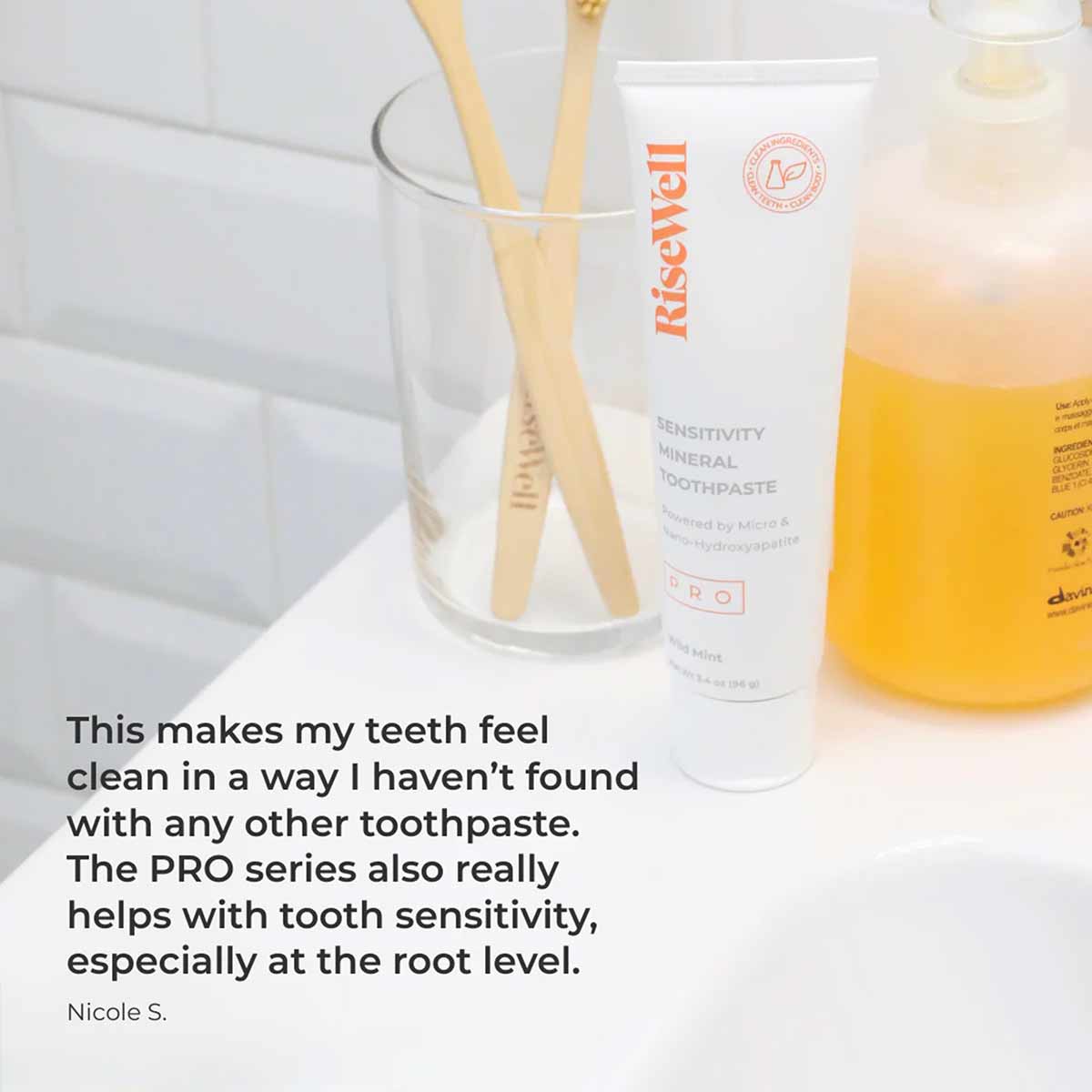 RiseWell Sensitivity Mineral Toothpaste tube on white surface with bamboo toothbrushes and bathroom items.