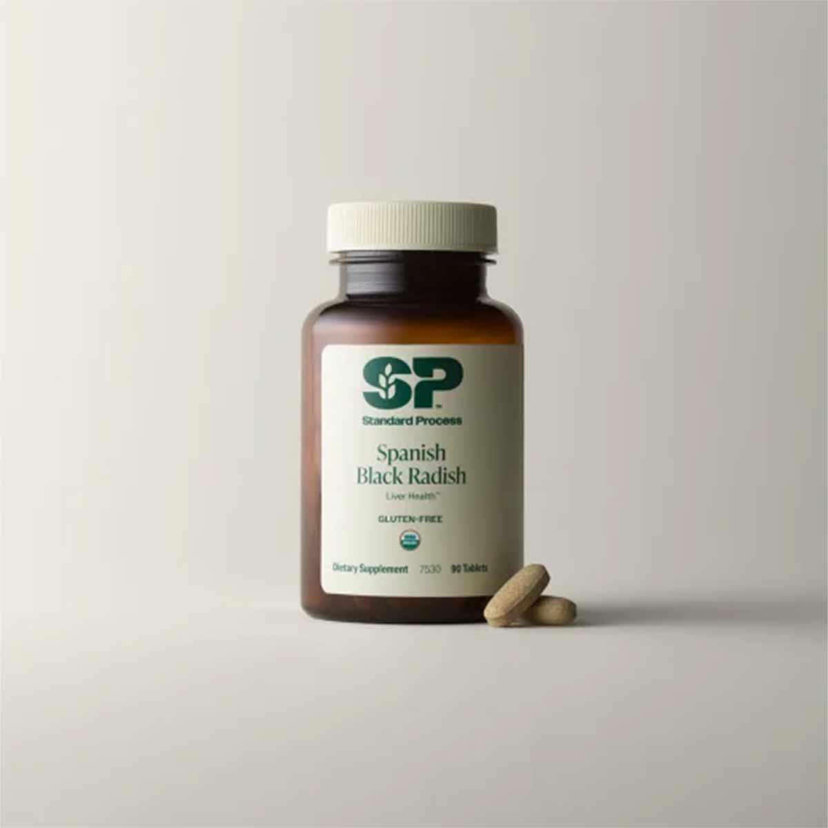 Brown glass bottle of Standard Process Spanish Black Radish dietary supplement with white cap and two tablets displayed besid