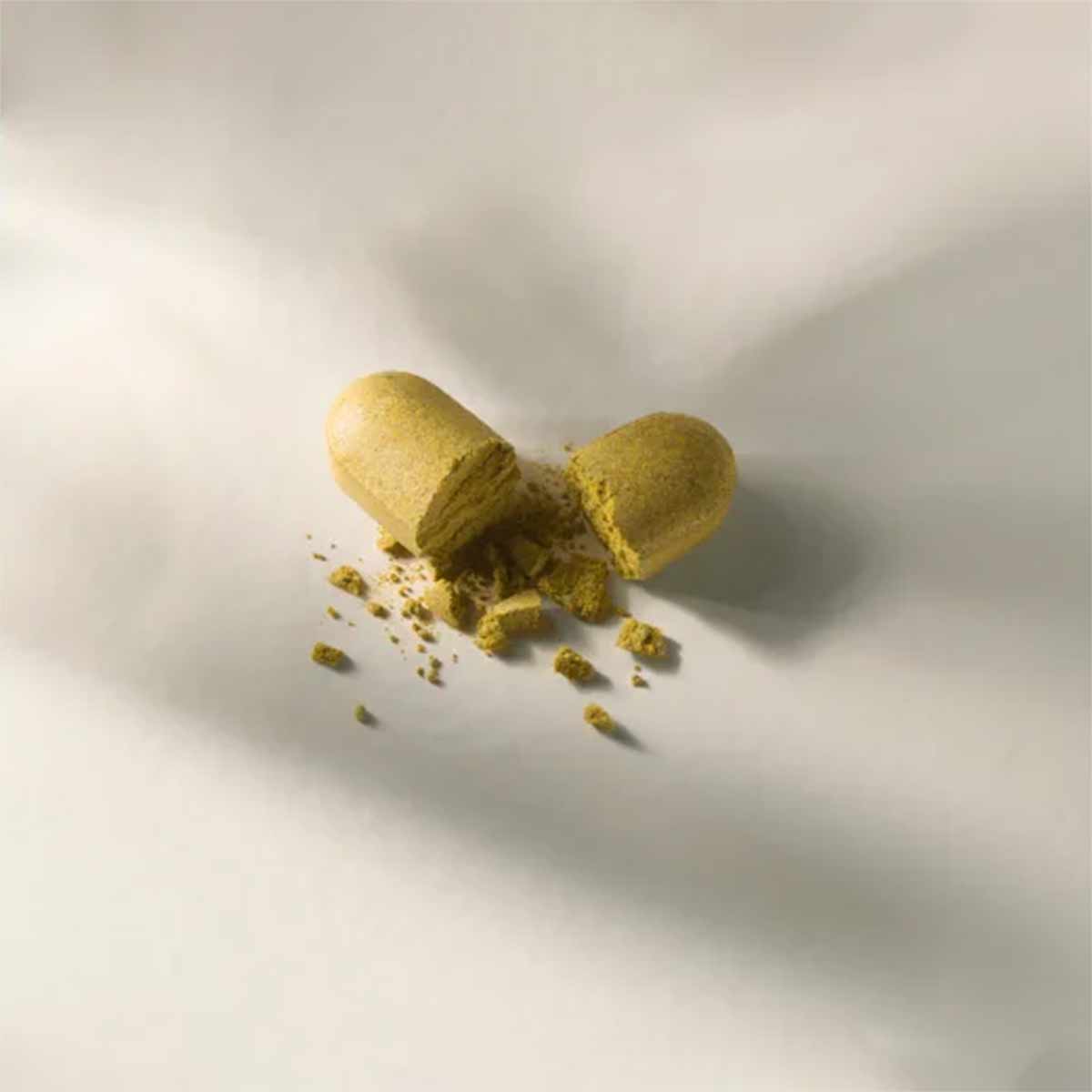 Two yellow-green capsules with powder spilling from an opened capsule on white background.