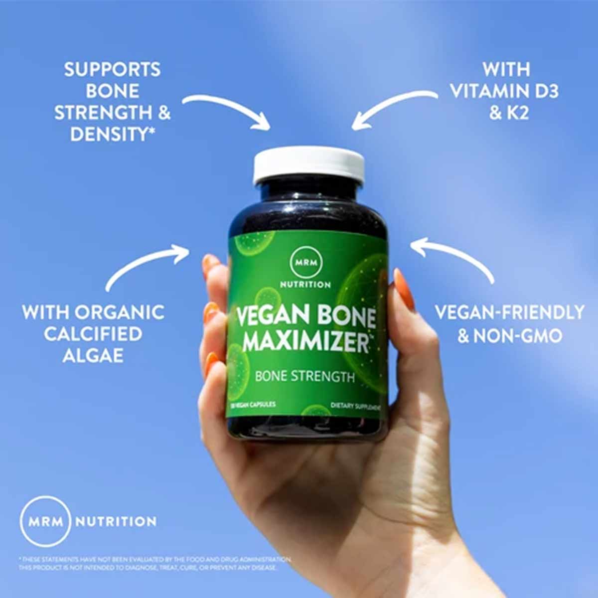 Hand holding dark glass bottle of MRM Vegan Bone Maximizer capsules with white cap against blue background.