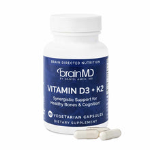 BrainMD Vitamin D3 + K2 supplement bottle with white cap and blue label, next to three vegetarian capsules.